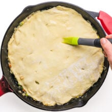 Vegan egg wash is being brushed over a pastry crust in a skillet.