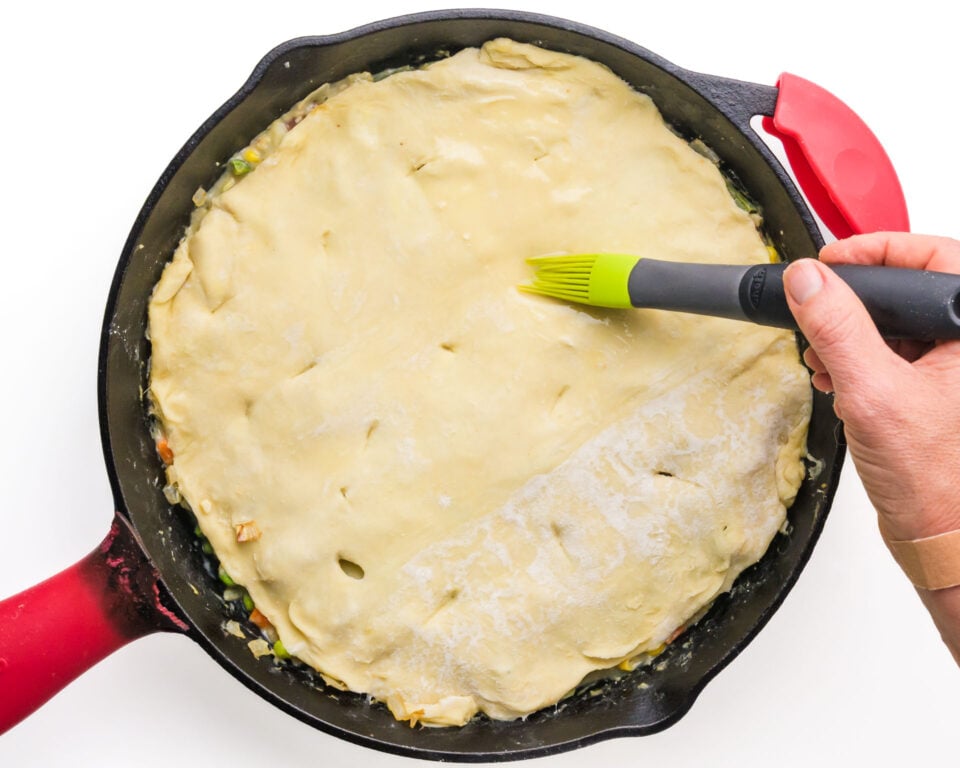 Vegan egg wash is being brushed over a pastry crust in a skillet.