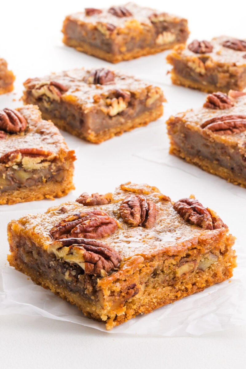 Several slices of pecan pie bars on a white table.