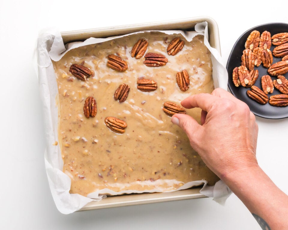 Pecans are being placed on top of pecan pie filling in a pan.
