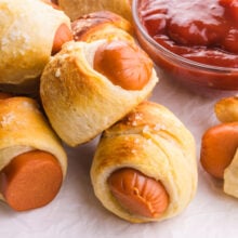 A vegan hot dog is wrapped in pastry next to several other and a bowl of ketchup.