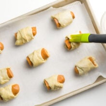 Vegan pigs in a blanket are being brushed with oat milk for browning.