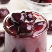A jar of cherry sauce is surrounded by fresh cherries.