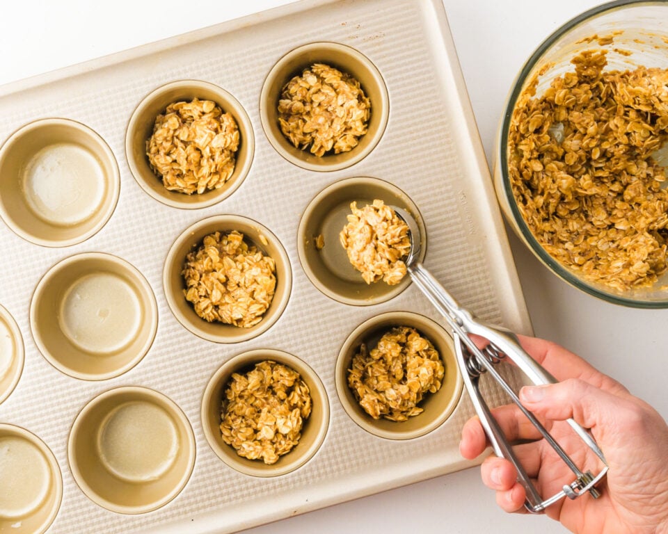 An oatmeal mixture is portioned into muffin pan compratments.