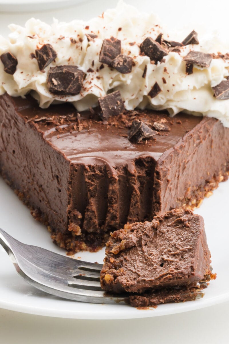 A slice of chocolate cream pie on a plate has a bite on a fork in front of it.
