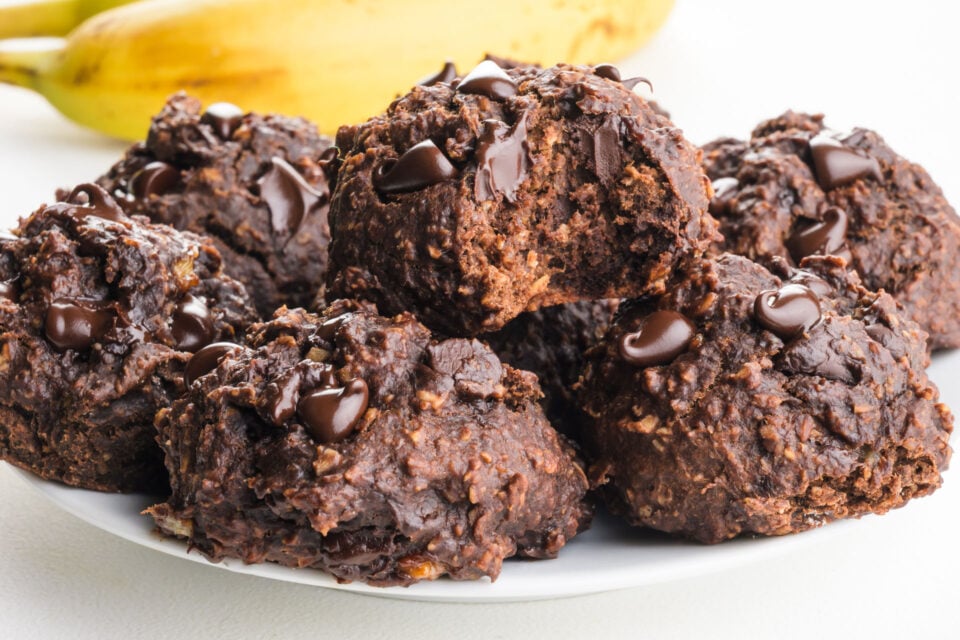 A plate of chocolate chip banana cookies shows the top one with a bite taken out.