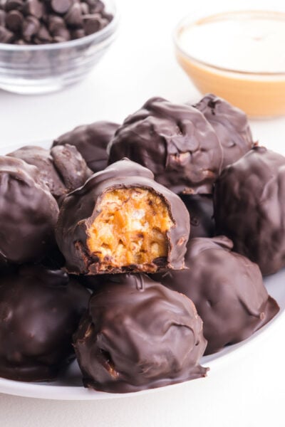 Several chocolate rice crispy peanut butter balls on a plate, one with a bite taken out.