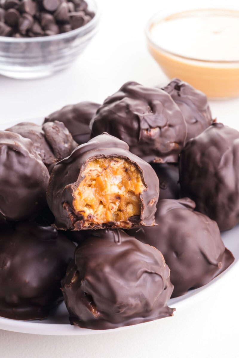 Several chocolate rice crispy peanut butter balls on a plate, one with a bite taken out.