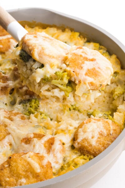 A serving of vegan chicken rice casserole is being dished from a skillet.