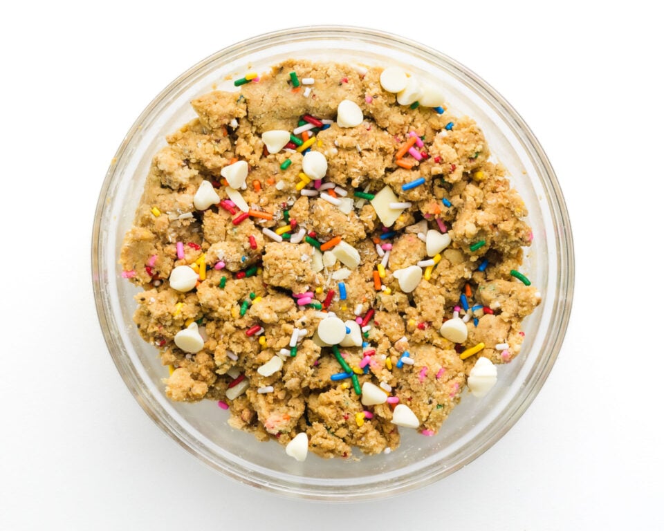 Bowl of cake batter protein ball dough with colorful sprinkles and white chocolate chips on a white background.