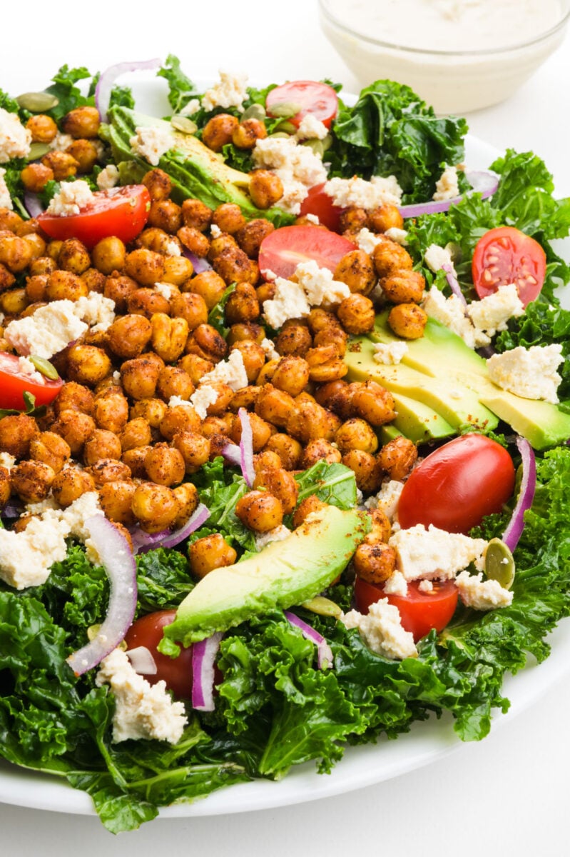A crispy, green chickpea kale salad has sliced avocado on top, along with cherry tomatoes and more veggies.