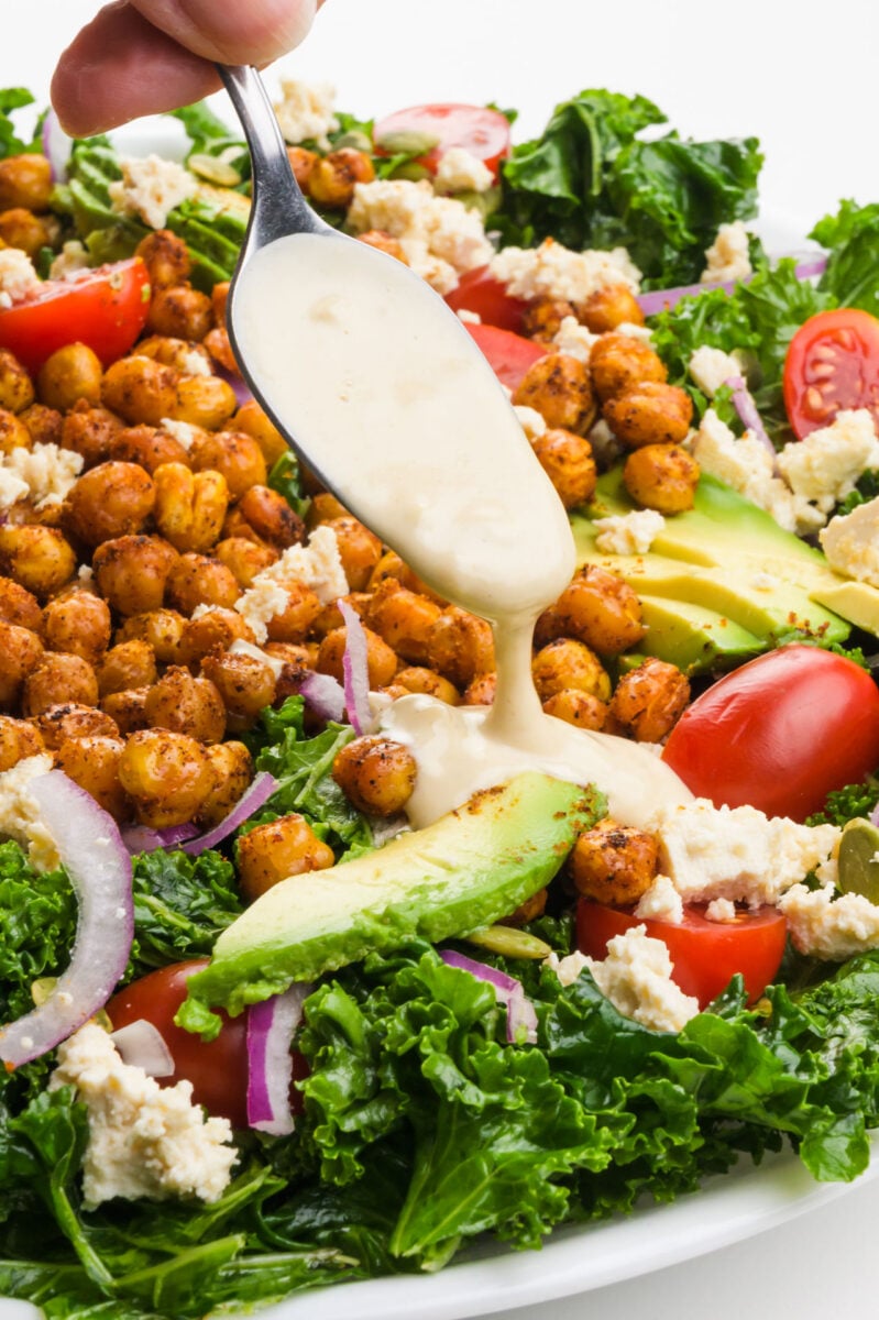 Dressing is being drizzled over a chickpea and kale salad.