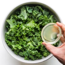 Lemon juice is being poured into a bowl with kale pieces.