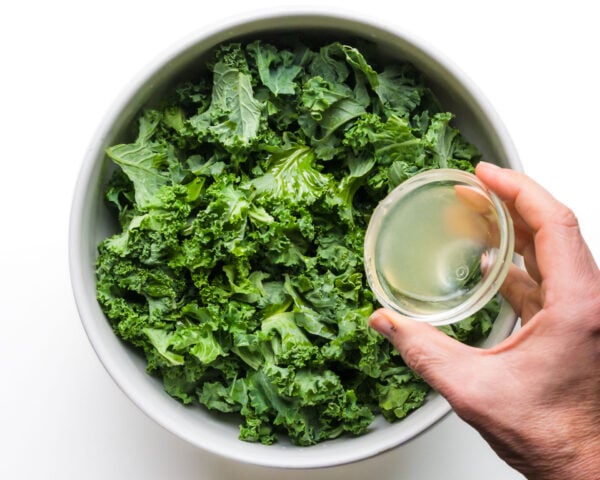 Lemon juice is being poured into a bowl with kale pieces.