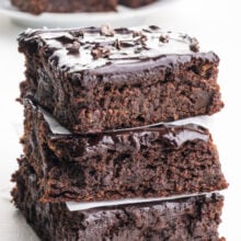 A stack of fudgy brownies with dates are topped with rich chocoalte frosting and cacao nibs.