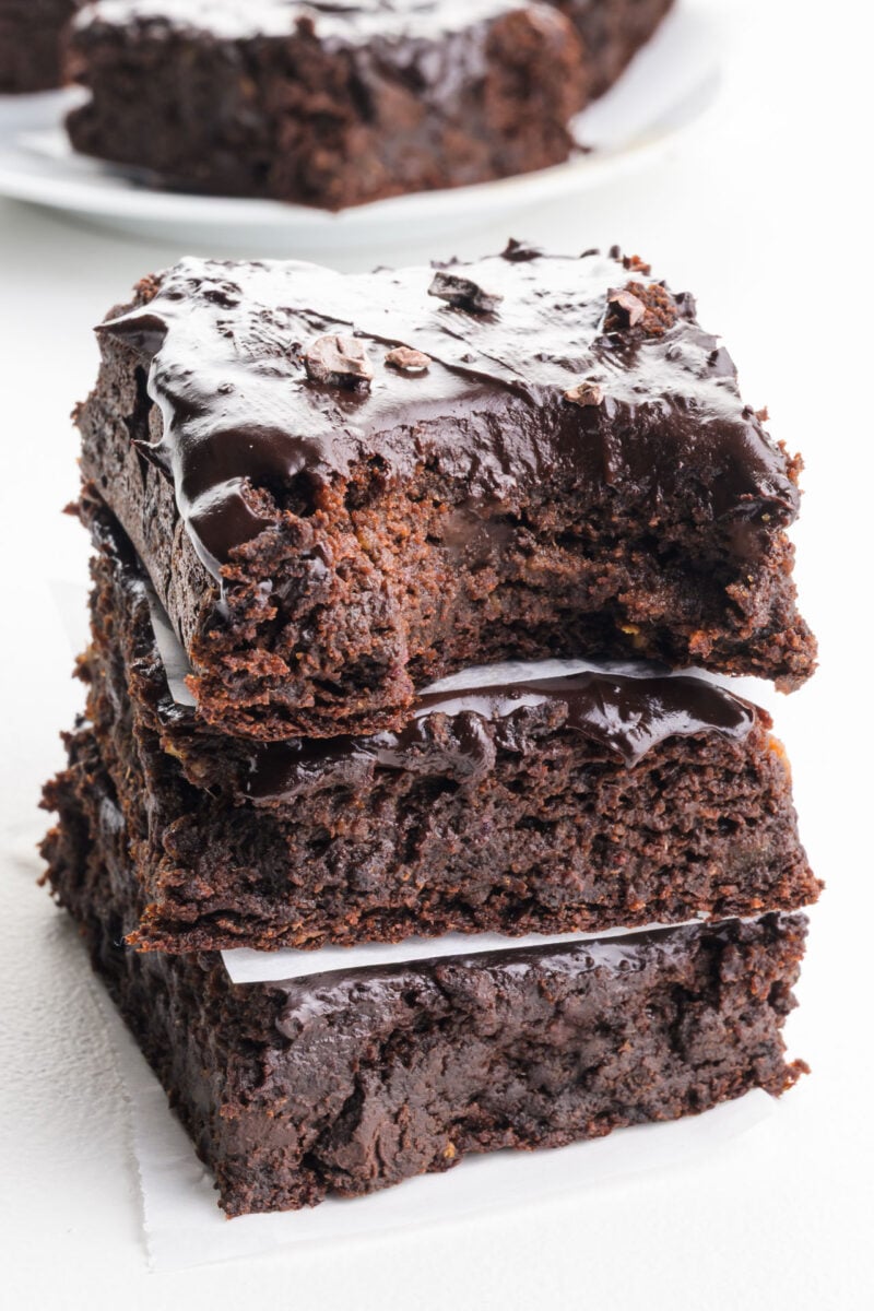 A close-up shot of several sliced fudgy date and chocolate brownies stacked on a white plate, showing a dense, moist texture with visible chocolate chips.