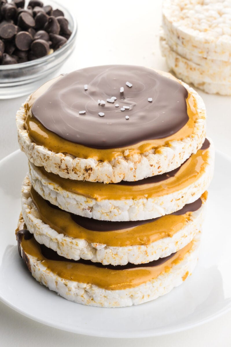 A stack of chocolate peanut butter rice cakes sit in front of chocolate chips and rice cakes.