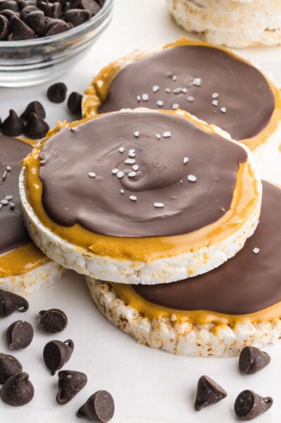 Several chocolate peanut butter rice cakes on a white table around chocolate chips.