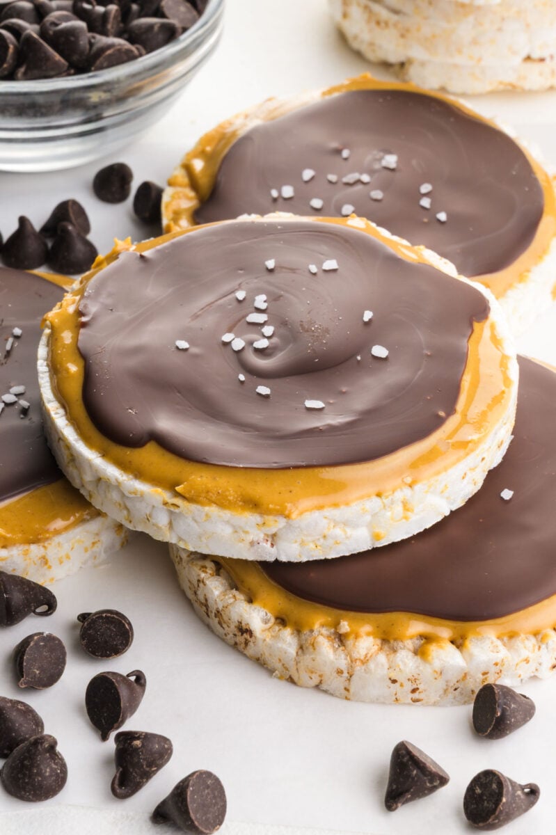 Several chocolate peanut butter rice cakes on a white table around chocolate chips.