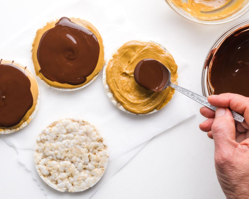 Chocolate sauce is being spread over a rice cake topped with peanut butter.