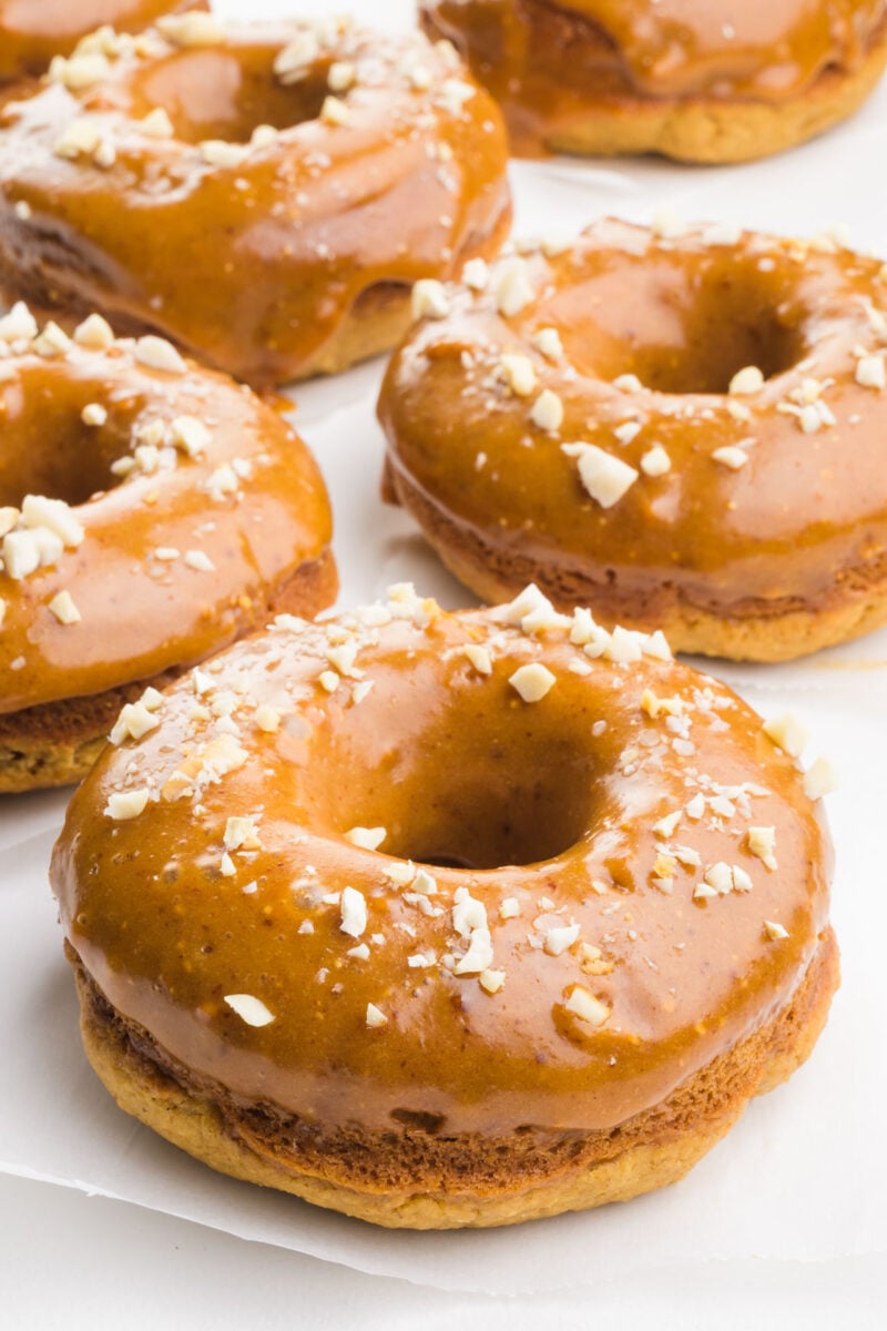 Several baked peanut butter donuts are all glazed and sitting on a white counter.