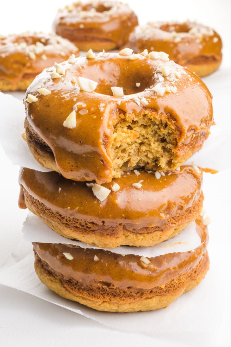 A stack of three peanut butter donuts with beautiful glaze shows the top one with a bite taken out.