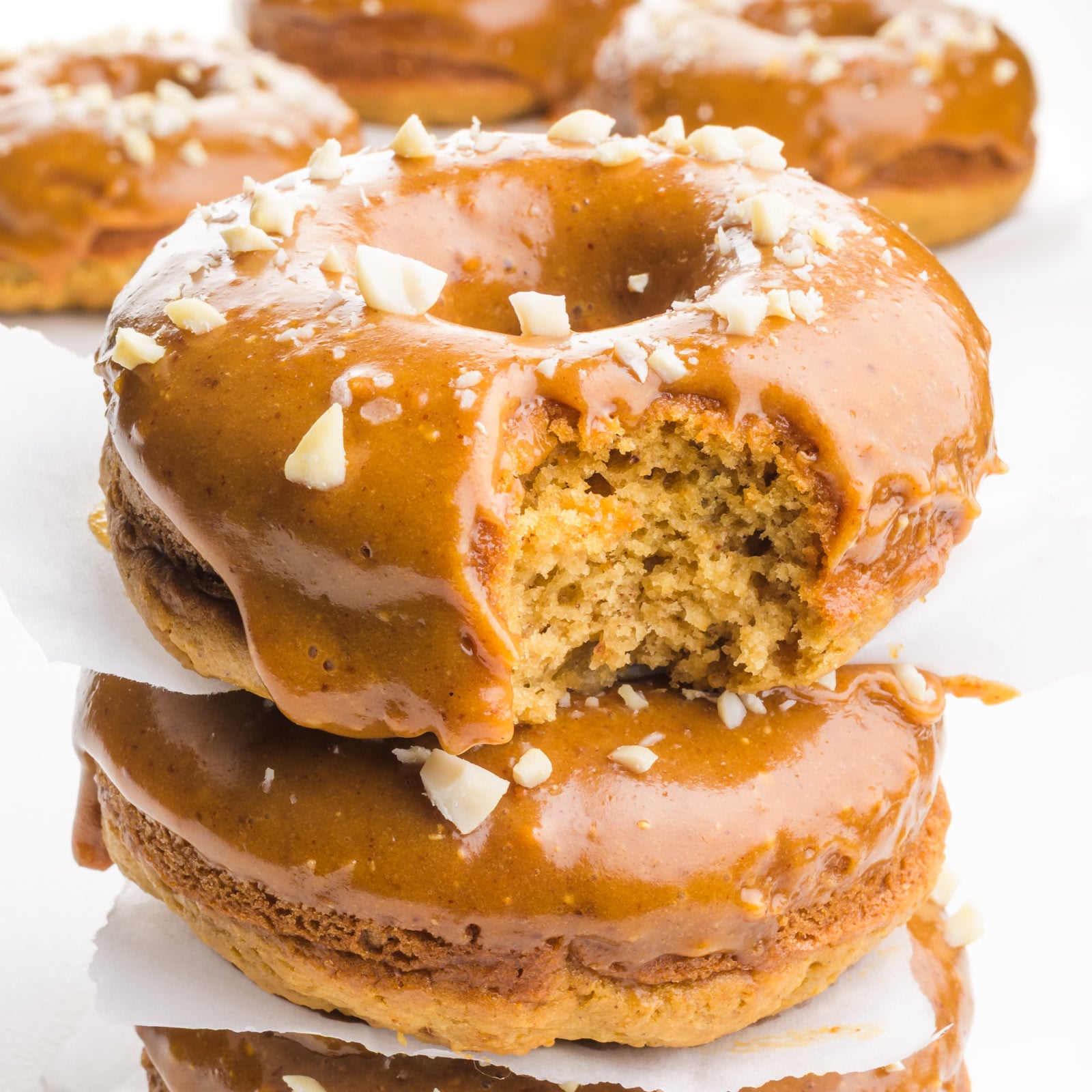 A closeup of a stack of donuts, all with peanut butter glaze, and the top one with a bite taken out.