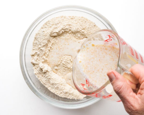 A milky mixture is being poured into a bowl with flour ingredients.