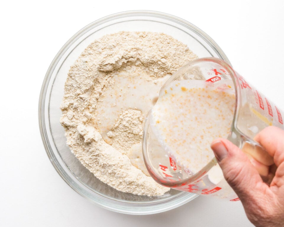 A milky mixture is being poured into a bowl with flour ingredients.