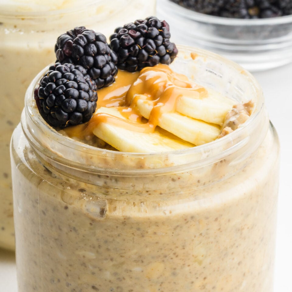 Overnight oats in a jar topped with sliced bananas, peanut butter drizzle, and blackberries.