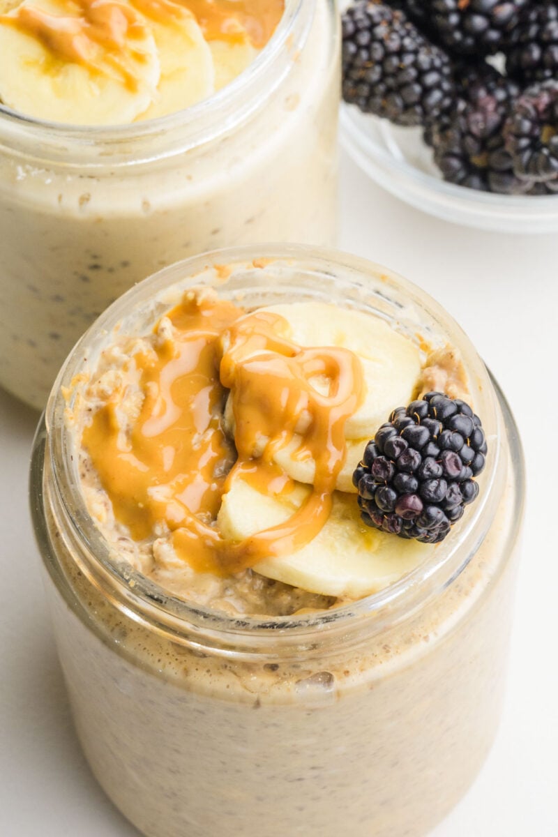 A jar of mashed banana peanut butter overnight oats is topped with peanut butter drizzles and fresh fruit.