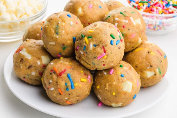 Colorful, ball-shaped protein birthday cake bites topped with sprinkles, stacked on each other.