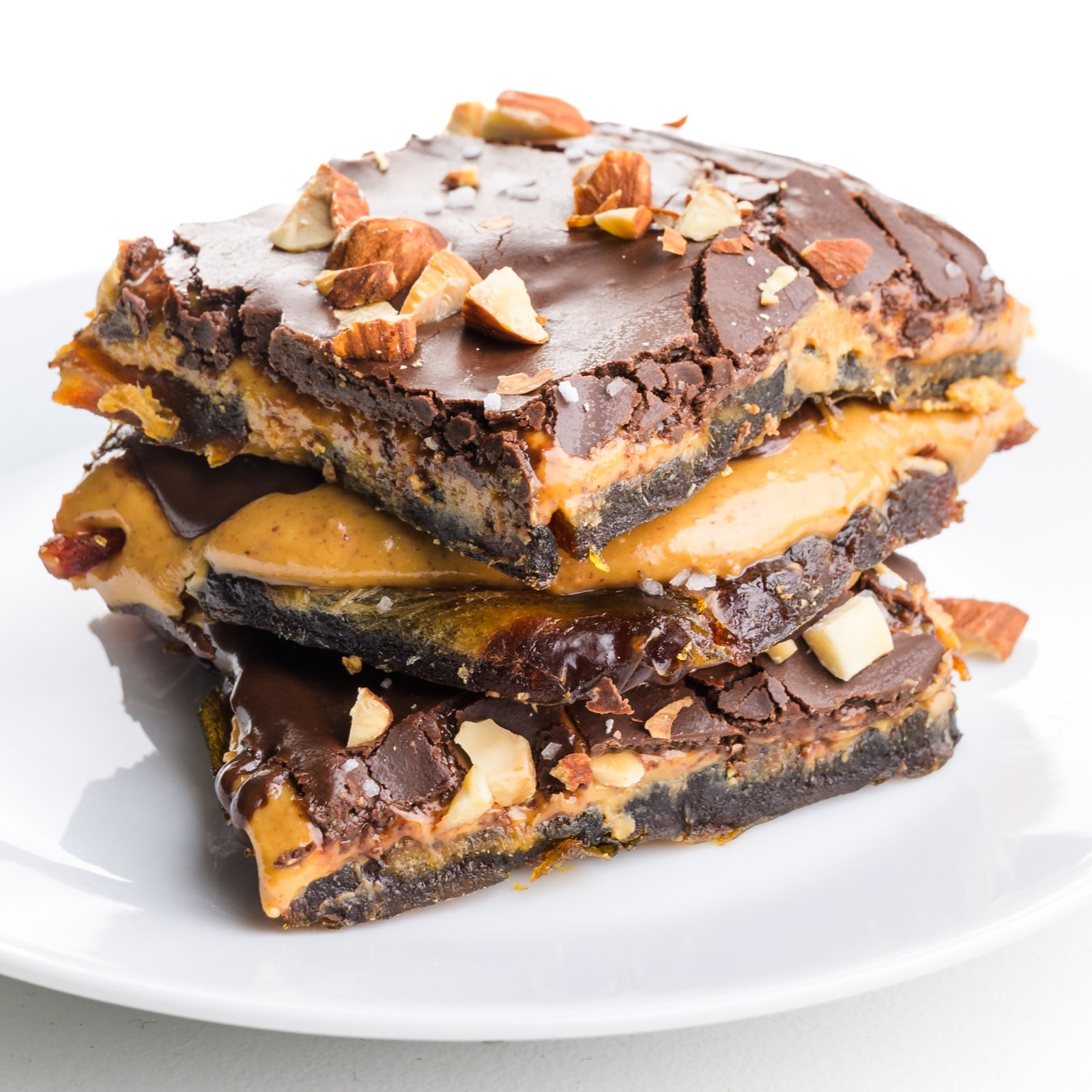 A stack of chocolate peanut butter bark slices are on a white plate with chopped almonds on top.
