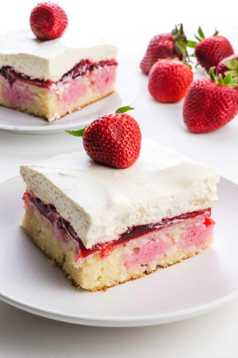 Vegan strawberry cake slice topped with a fresh strawberry, served on a white plate.