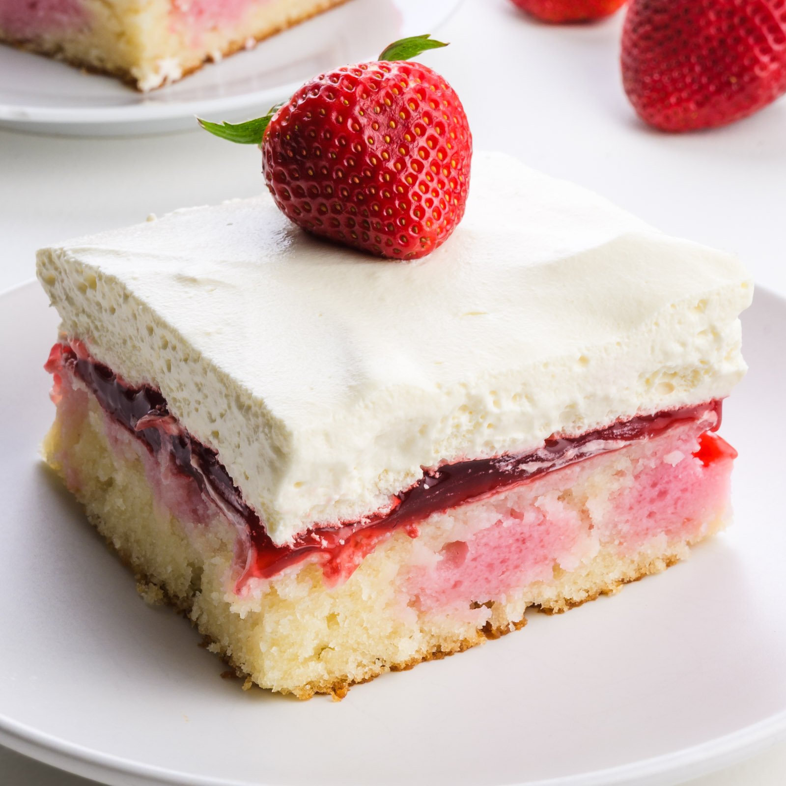 Vegan strawberry cake slice topped with a fresh strawberry, served on a white plate.