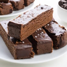 Chocolate layered protein bars topped with glossy chocolate and a sprinkle of sea salt, served on a white plate.