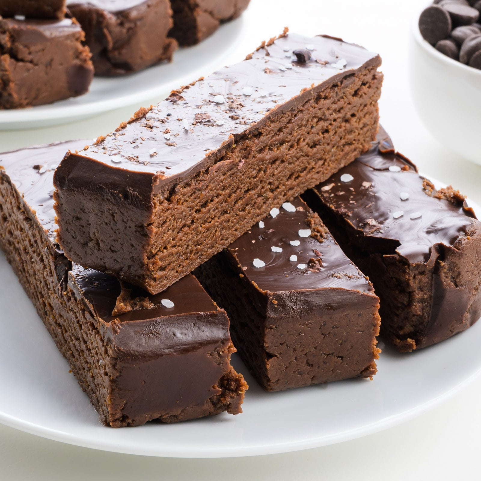 Chocolate layered protein bars topped with glossy chocolate and a sprinkle of sea salt, served on a white plate.