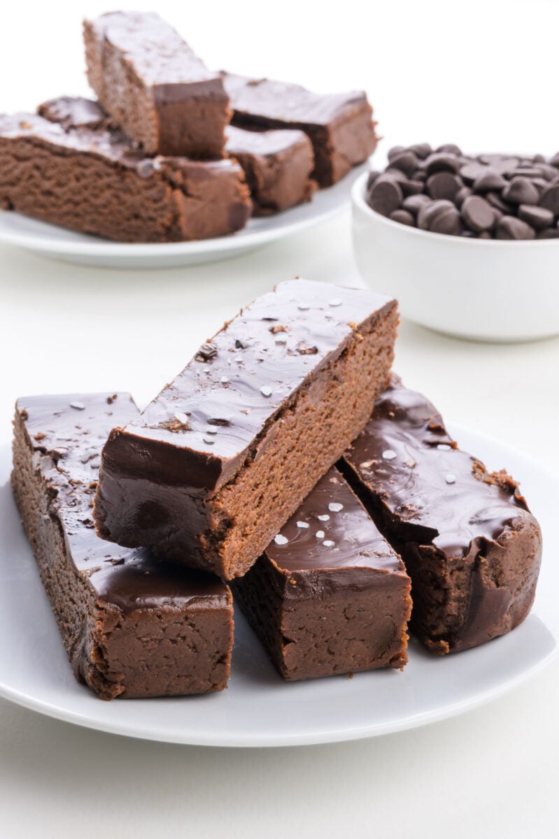 Chocolate protein bars with a glossy coating and a sprinkle of sea salt, accompanied by a bowl of chocolate chips.