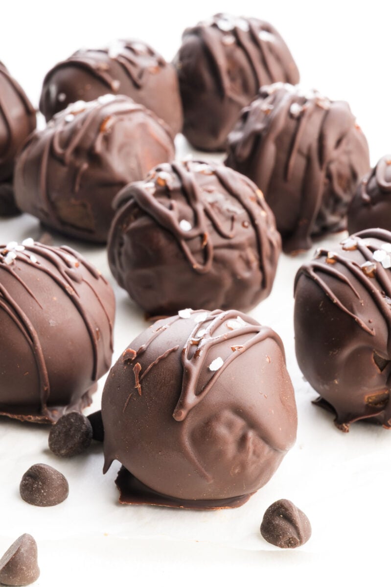 Chocolate truffles drizzled with dark chocolate and topped with coarse salt, arranged on a white surface.