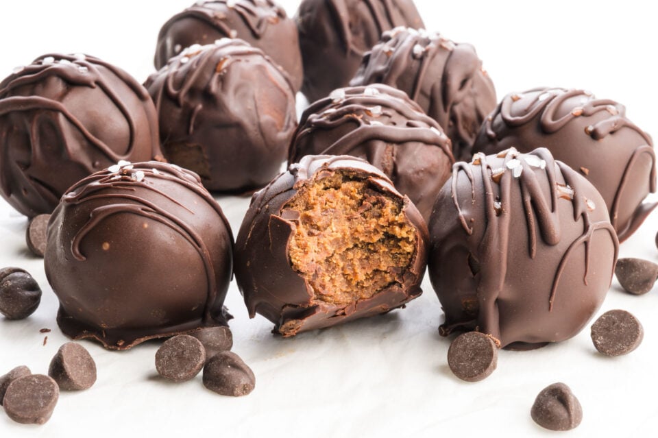Chocolate truffles with a bite taken out, revealing a creamy filling, surrounded by whole truffles and chocolate chips.