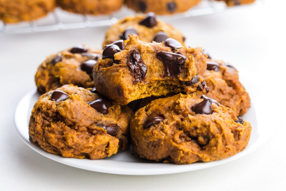 Plate of pumpkin chocolate chip cookies, some broken to show soft interior and melted chocolate chips.
