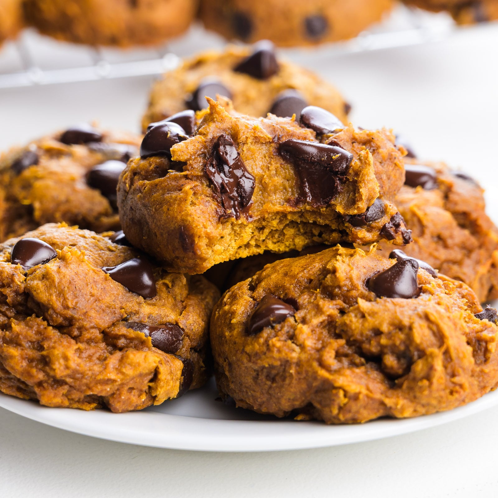 Plate of pumpkin chocolate chip cookies, some broken to show soft interior and melted chocolate chips.
