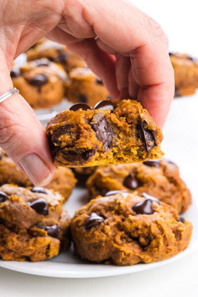 Plate of soft pumpkin cookies with chocolate chips, some with bites taken out, on a white background.