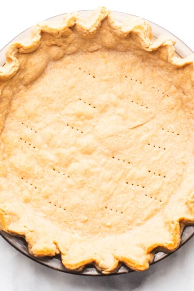 Raw pie crust in a round dish with a fluted edge and pricked surface.